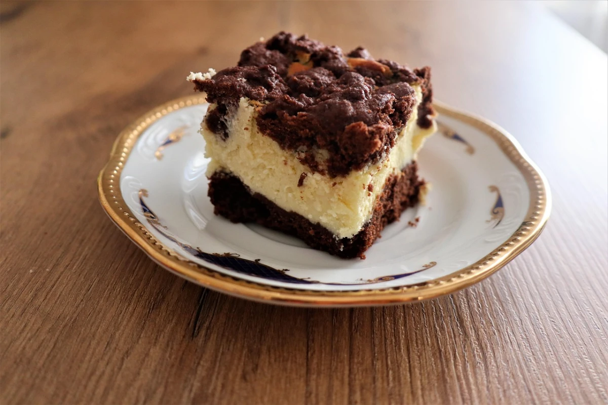 Kawałek sernika z czekoladową kruszonką i czekoladowym spodem, leży na ozdobnym talerzyku